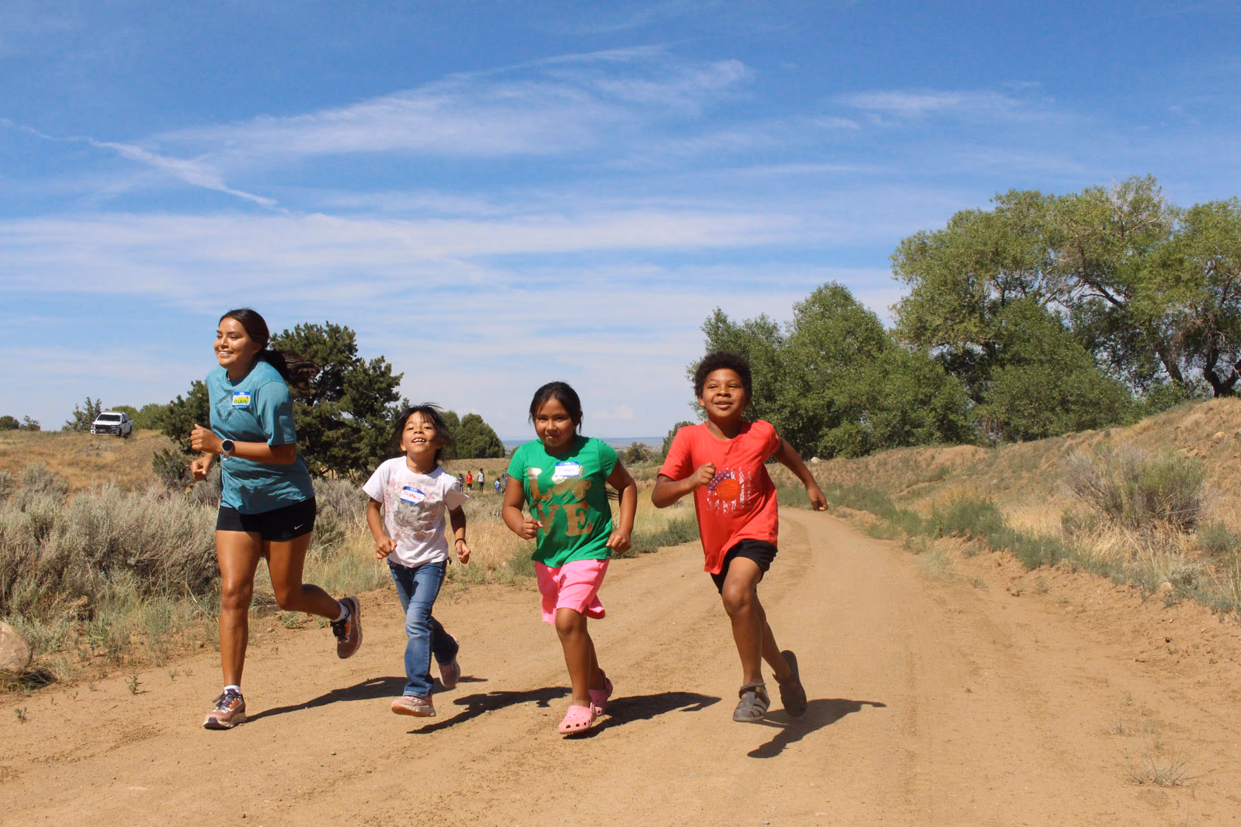 A Wings mentor runs alongside three Native youth on a dirt trail under a blue sky